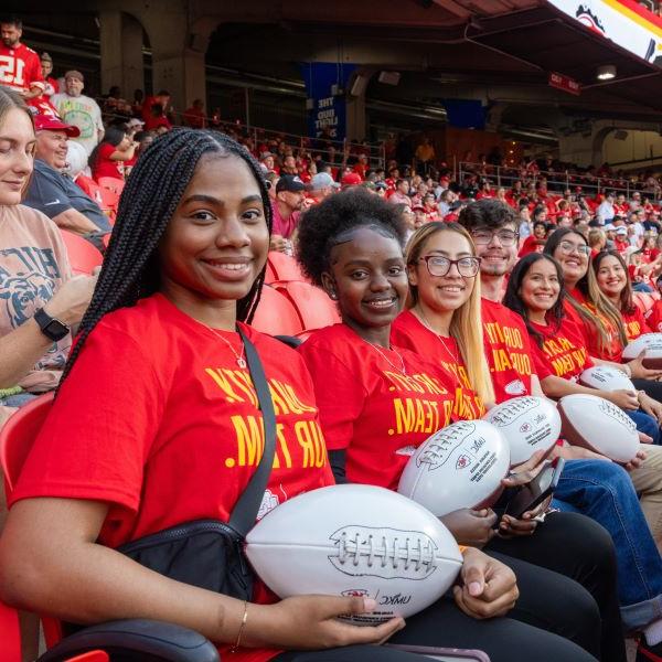 UMKC students dressed in Chiefs red t-shits sit in seats at the stadium after being celebrated on the field.